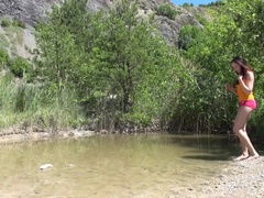 Susan plays with her wet pussy sitting on a rock at a secluded lake